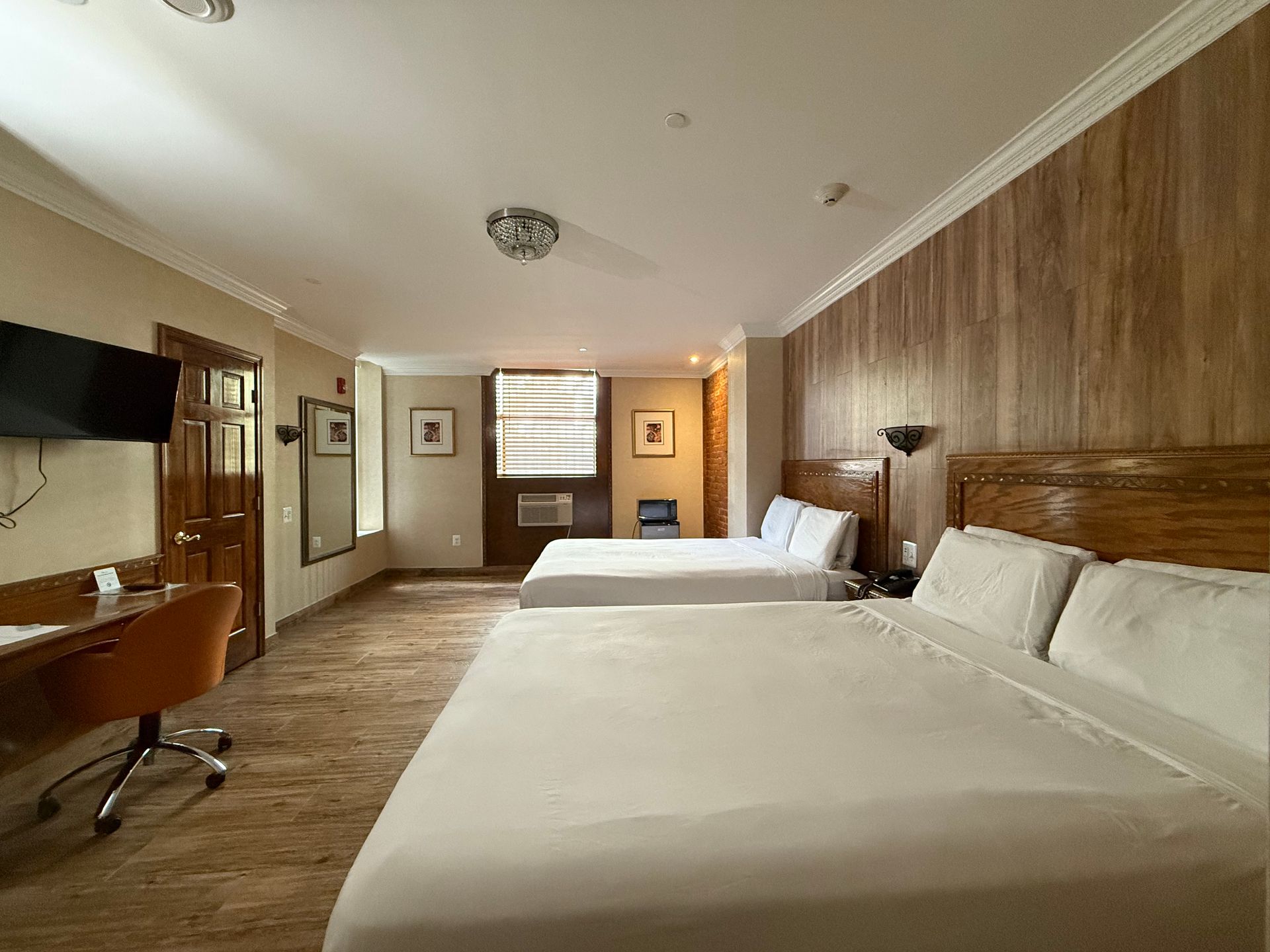 Hotel room with two beds, a desk, TV, and wood-paneled accent wall.