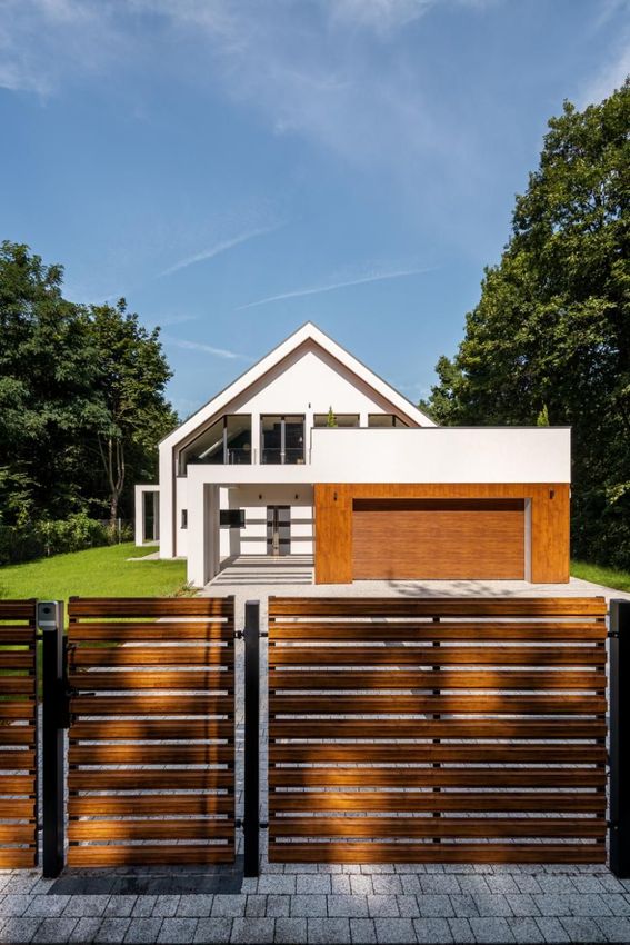 White modern house with wooden garage door, behind a wooden slat fence.