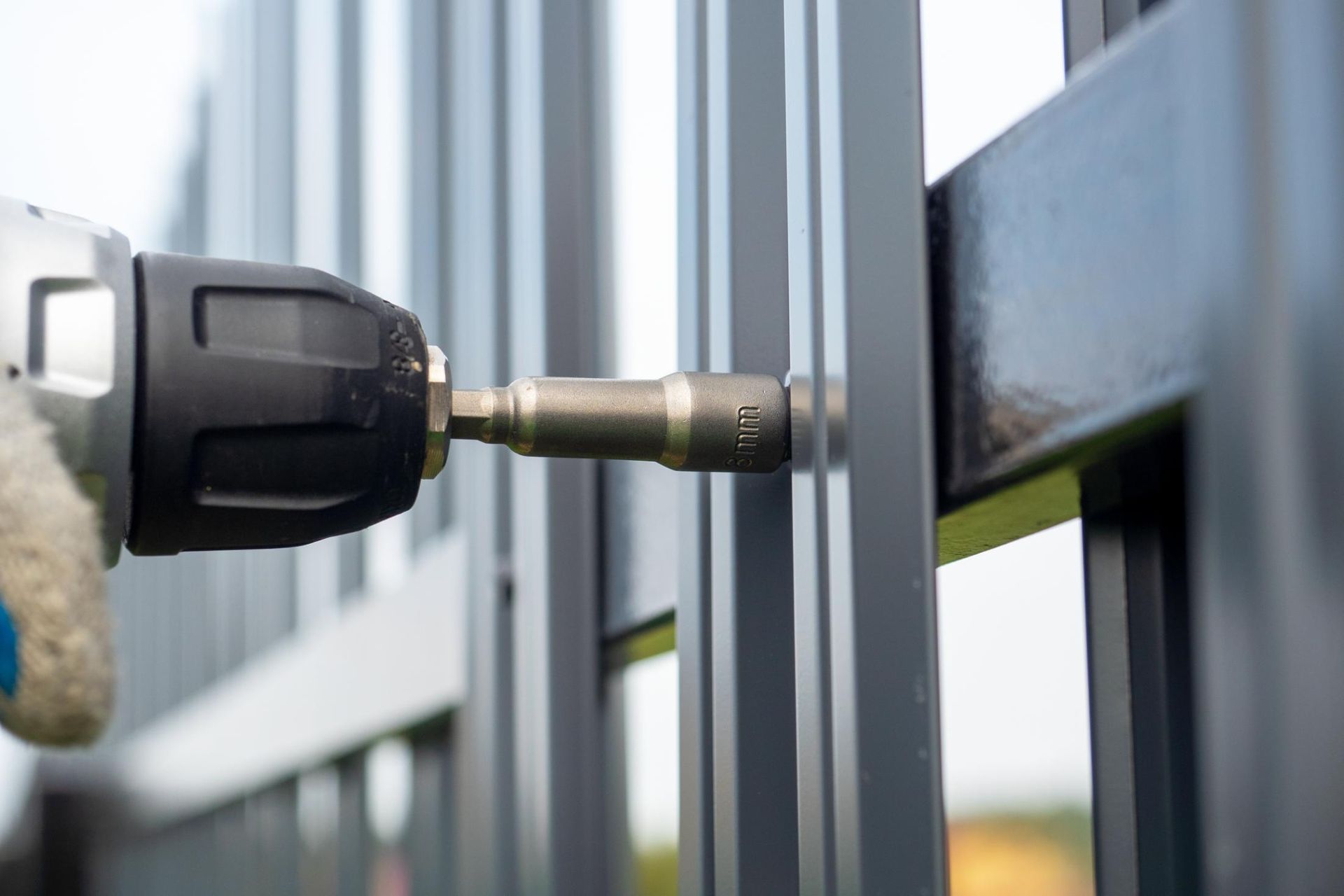 A person with a drill, attaching metal fence pieces together.