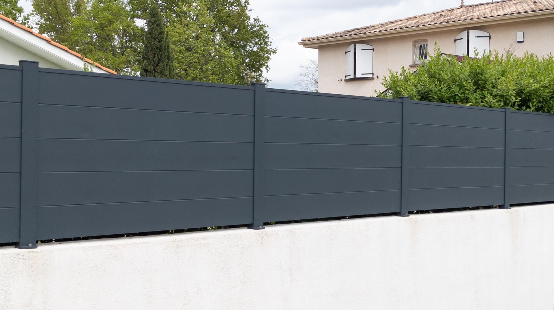 Gray horizontal slat fence atop a white wall, separating two houses.
