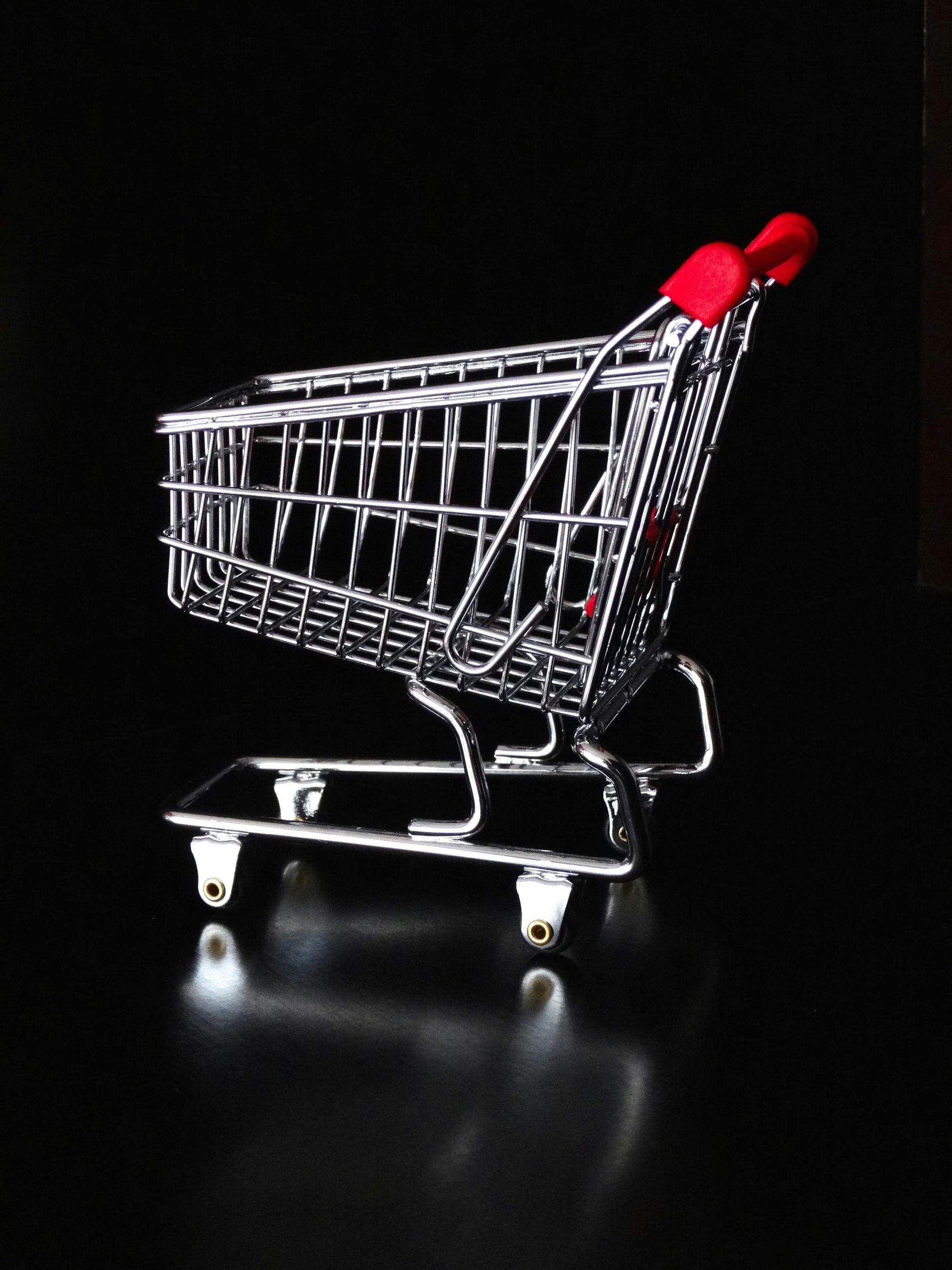 Mini shopping cart with red handles on a black background, lit from above.