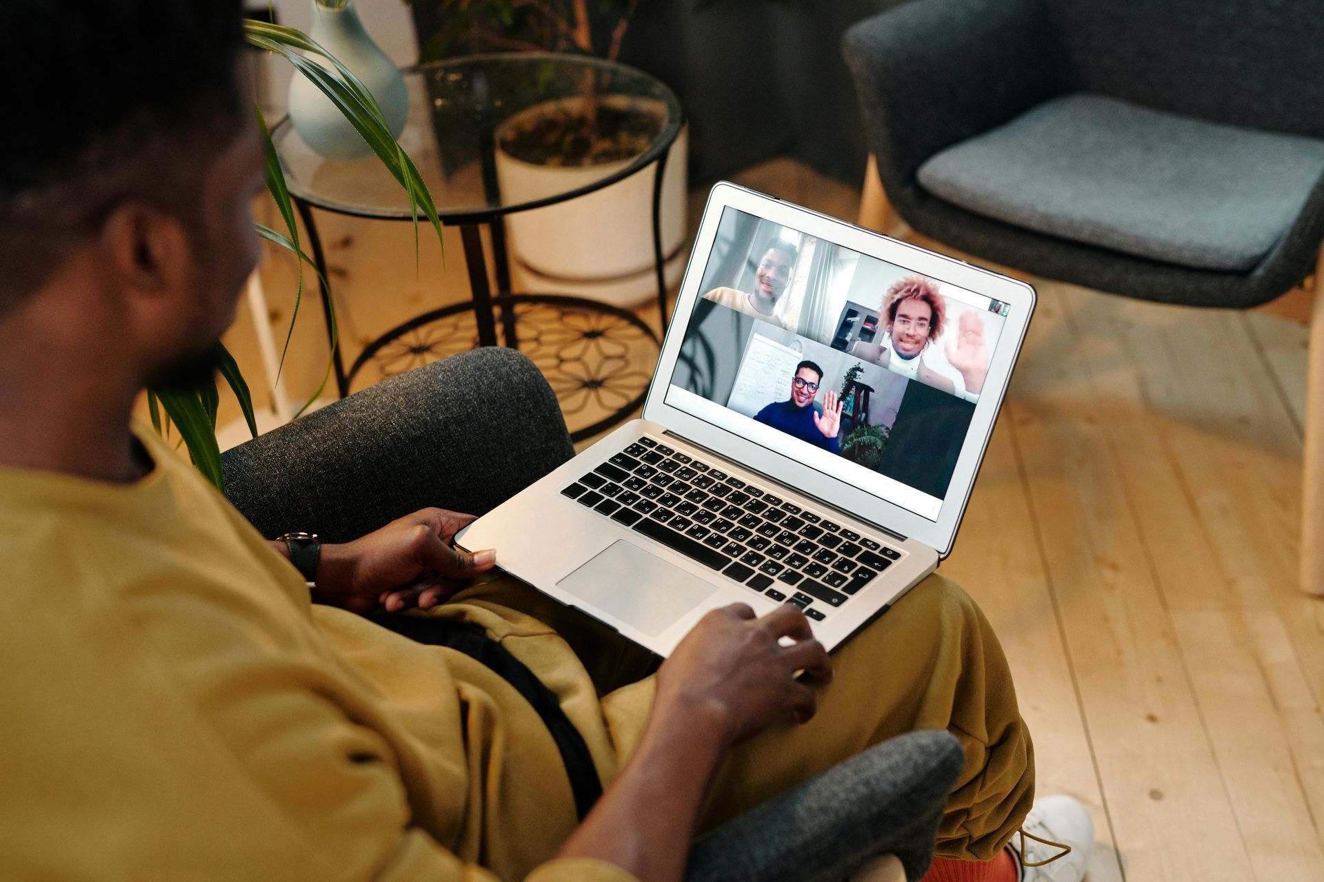 Person on a laptop video call while seated indoors with coffee and a plant nearby