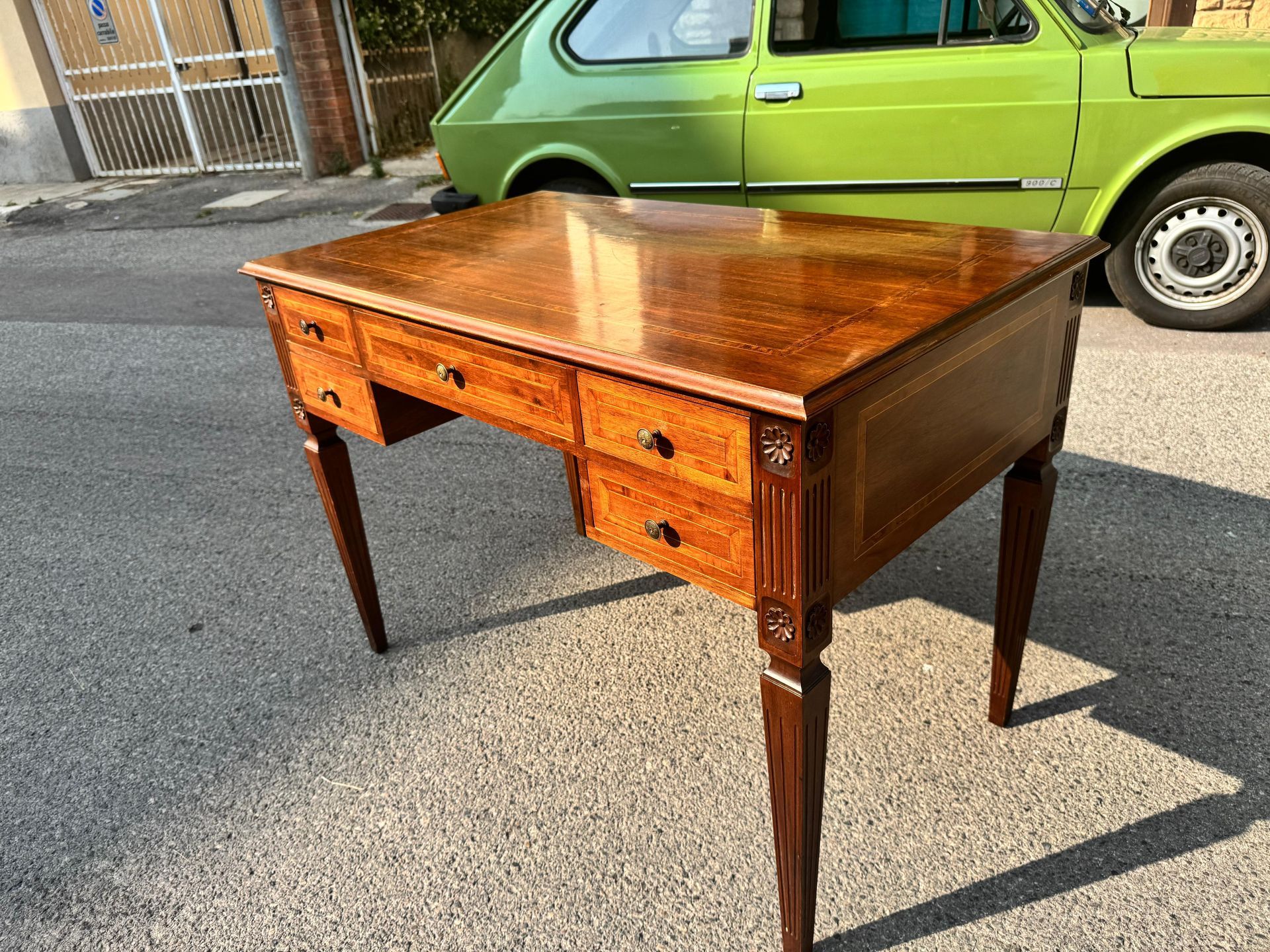 Una scrivania di legno con cassetti è parcheggiata davanti a un'auto verde.