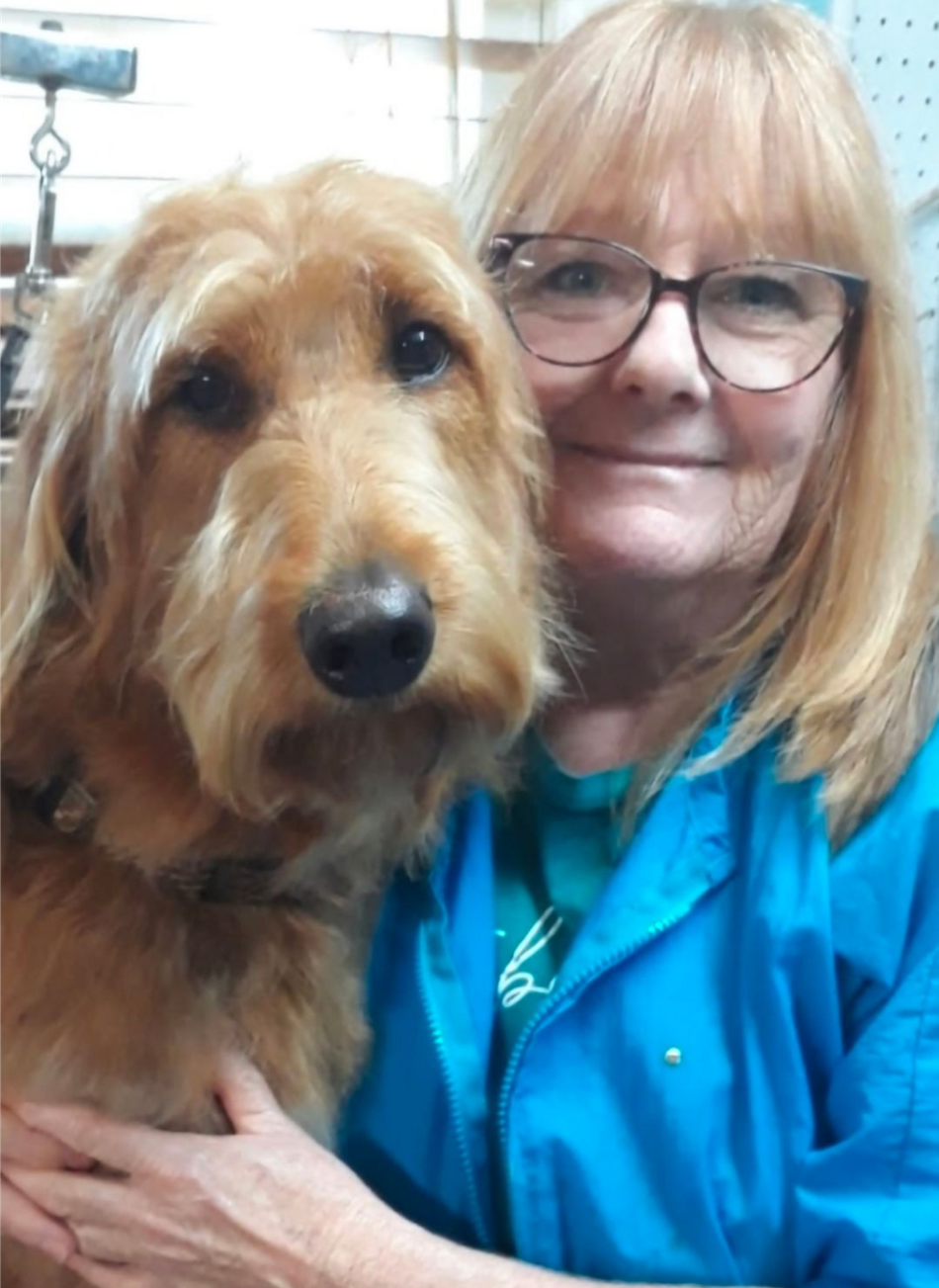 Woman in blue jacket holding a tan dog, both facing the camera and smiling.