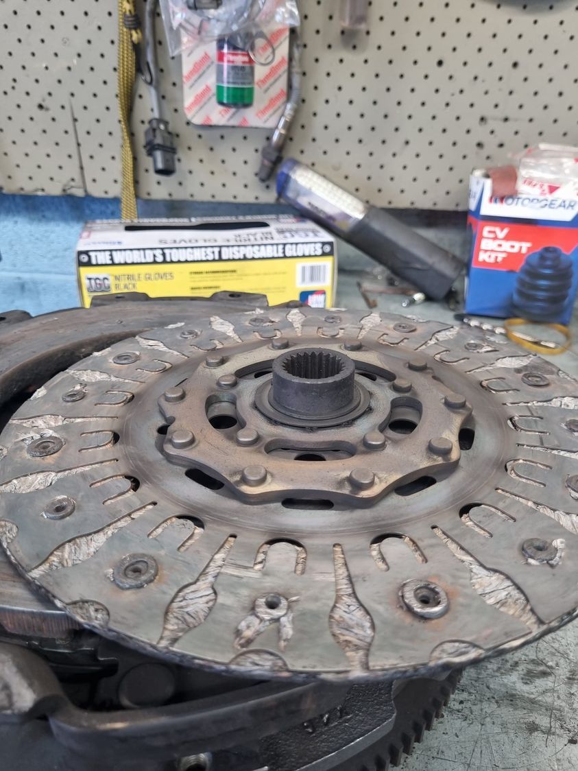 Worn Clutch Disc Sitting on A Flywheel, with Parts and Tools on A Workbench — Erina Mechanical Repairs In Erina, NSW