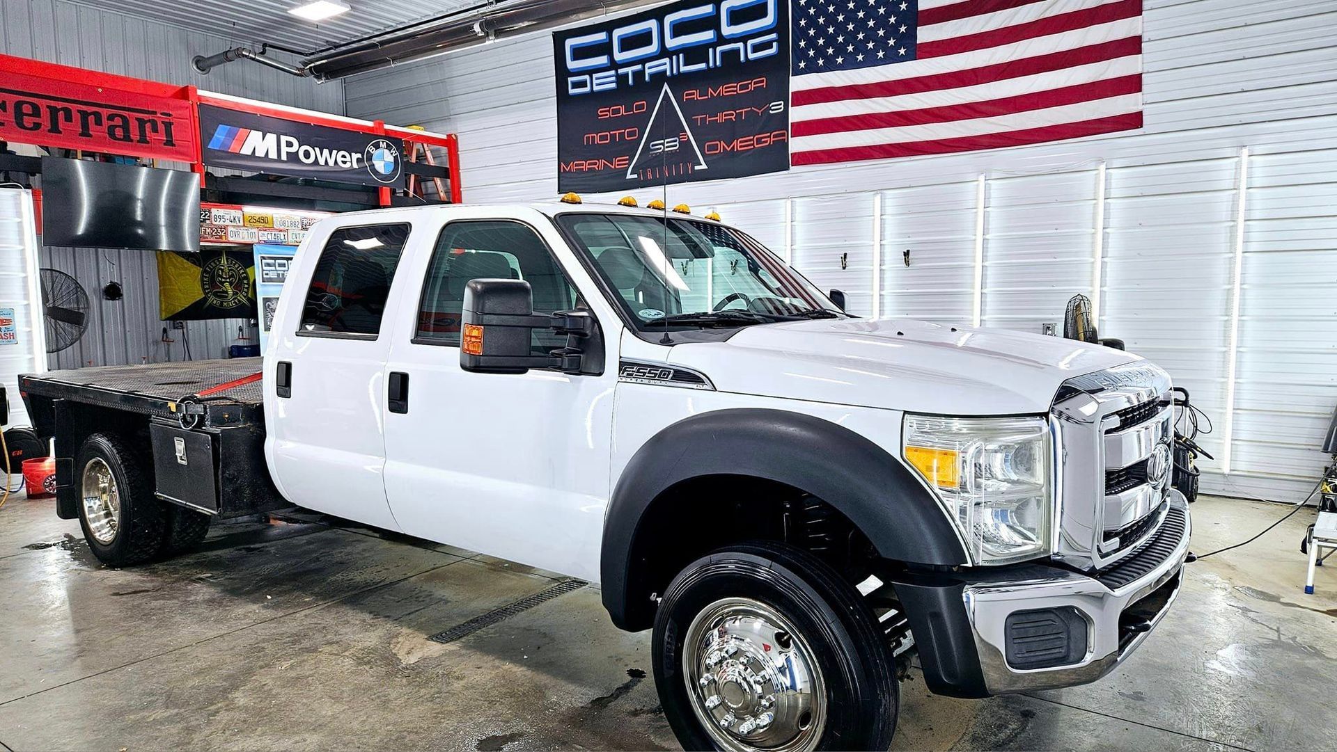 A white tow truck is parked in a garage next to an american flag.
