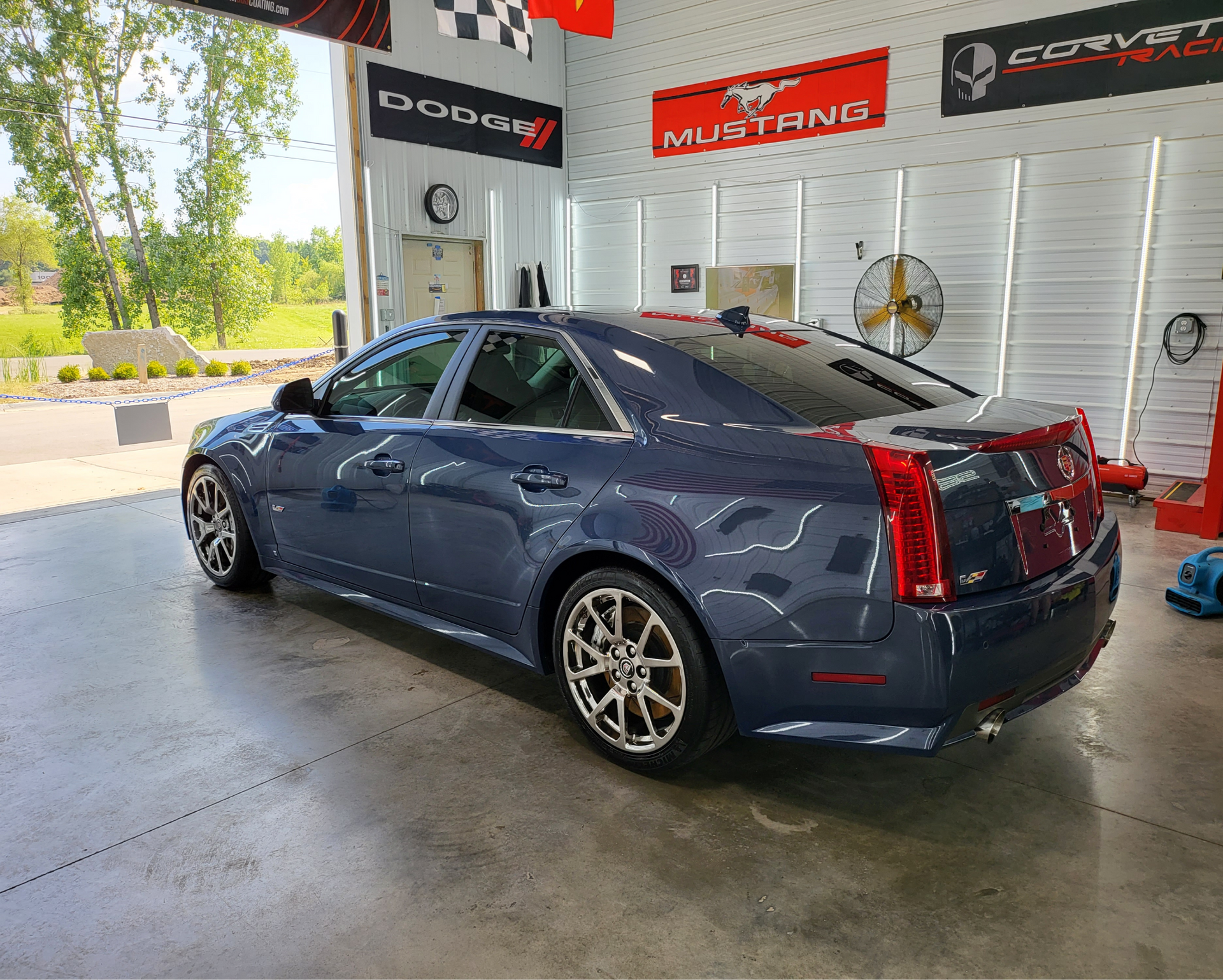 A blue car is parked in a garage with a mustang sign on the wall.