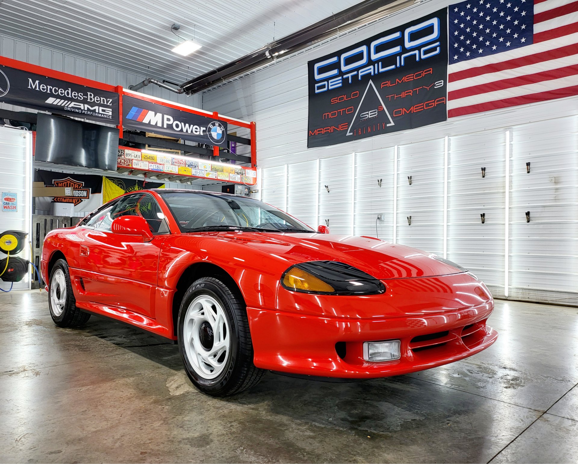 A red sports car is parked in a garage next to an american flag.