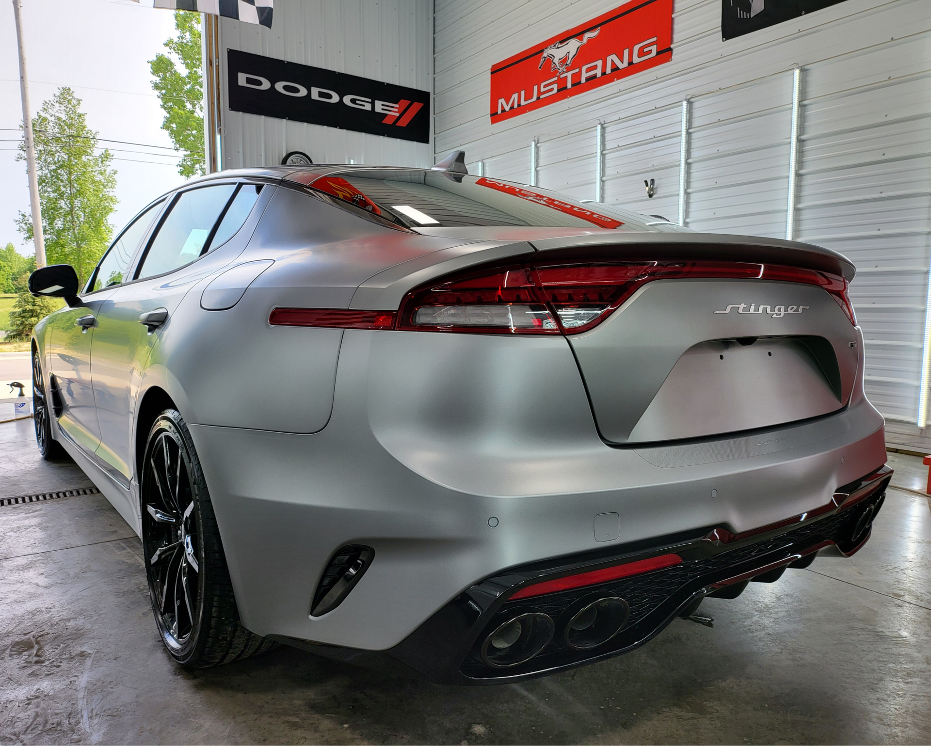 A silver mustang is parked in a garage next to a dodge sign.