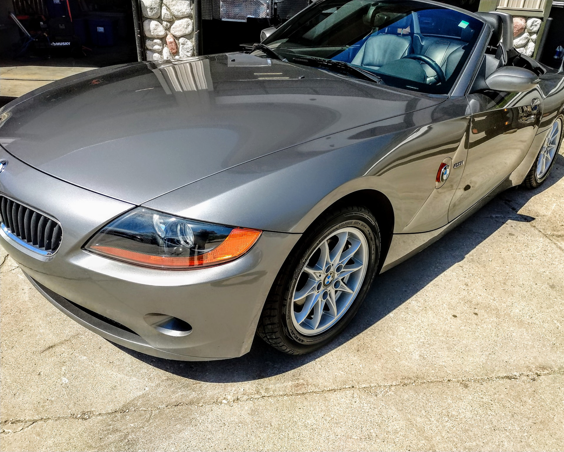 A silver bmw z4 convertible is parked in front of a garage door.