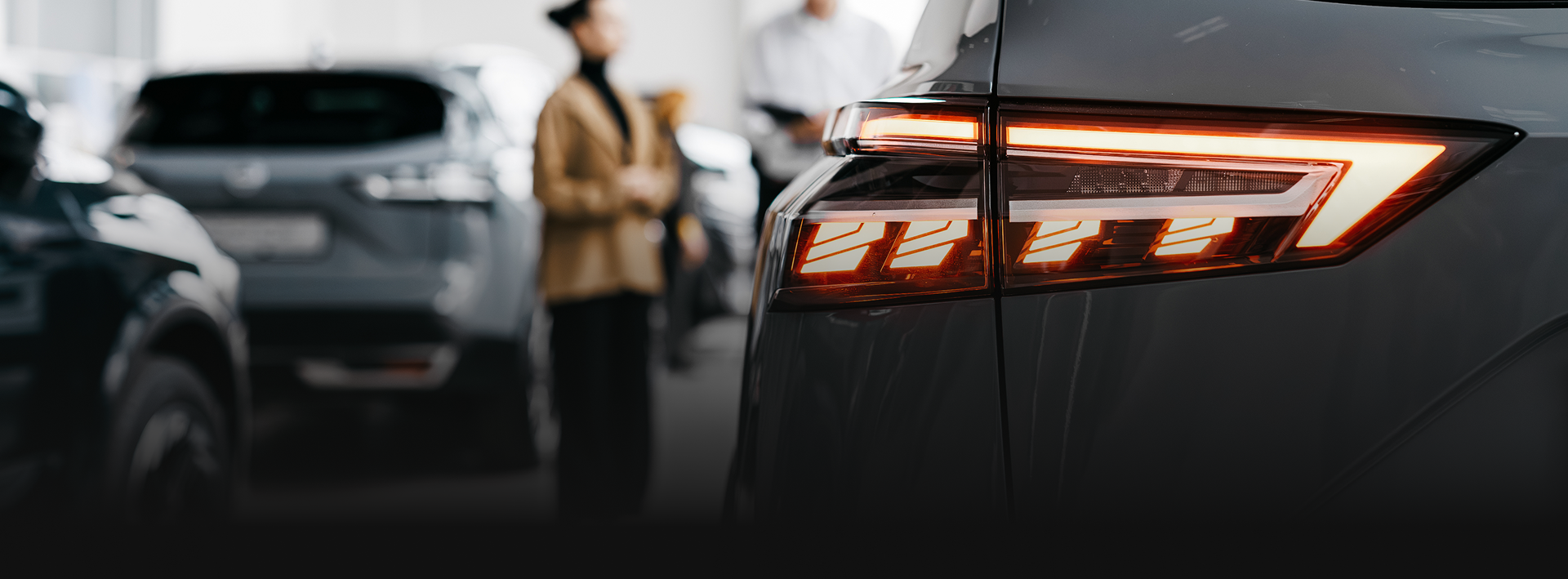 Close-up of a car’s illuminated taillight in a parking lot, with blurred vehicles in the background