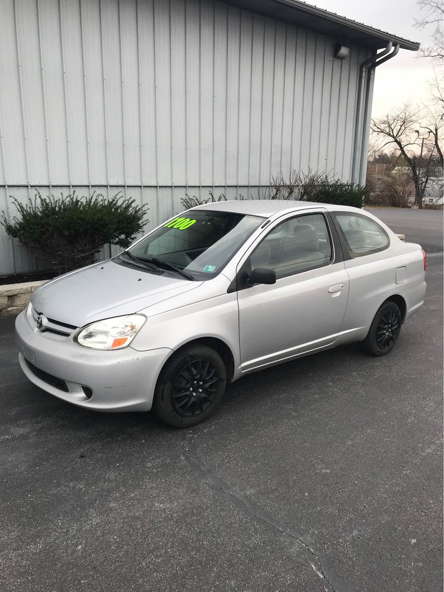 Silver Toyota Echo coupe parked near a building; black wheels.