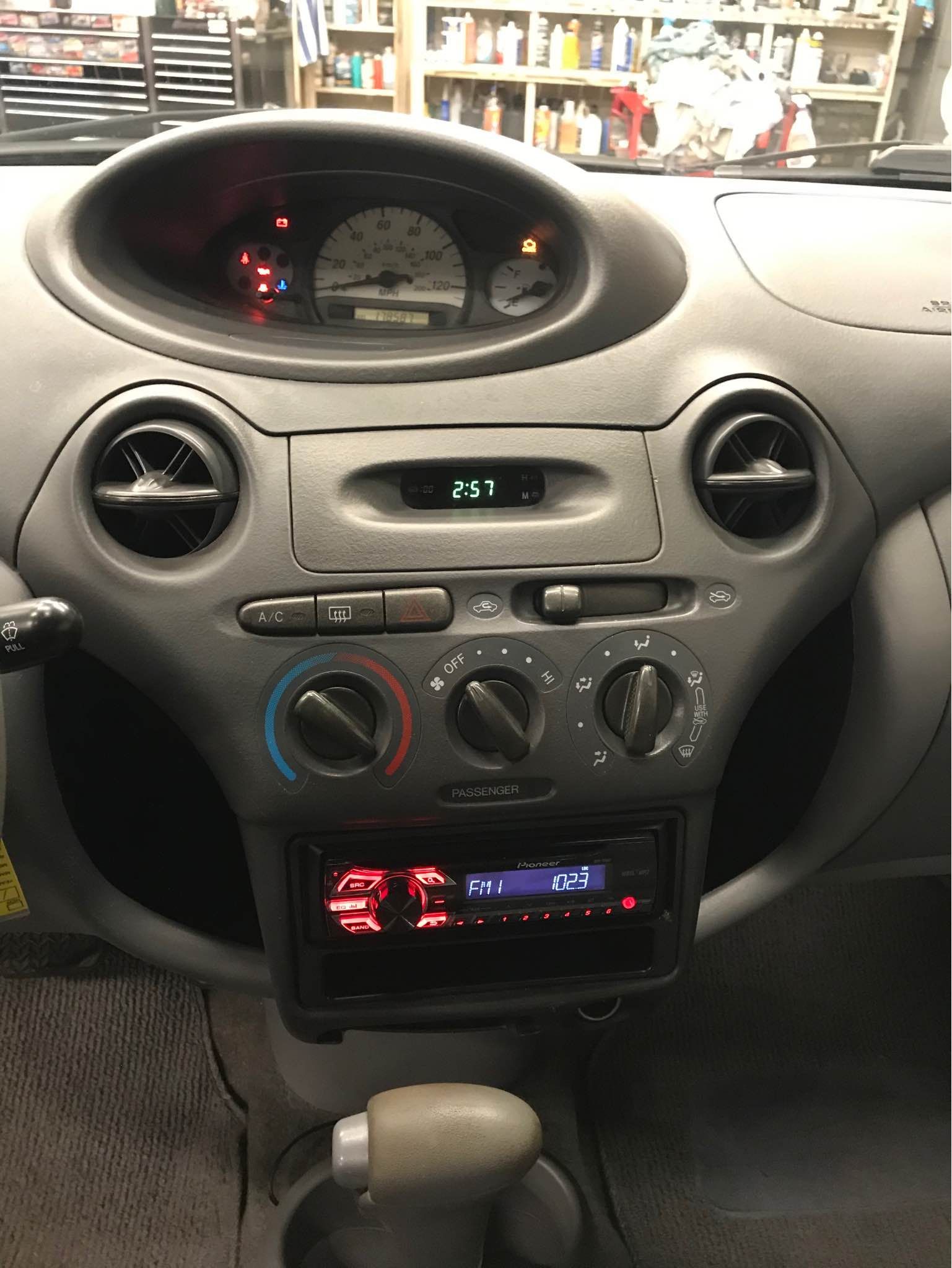 Car dashboard: speedometer, vents, radio, climate controls; grey and black with illuminated displays.
