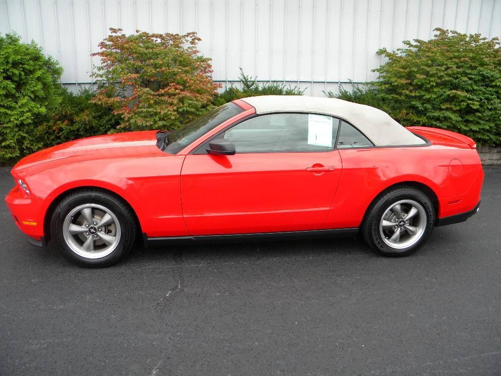 Red convertible car with a tan top parked on asphalt.