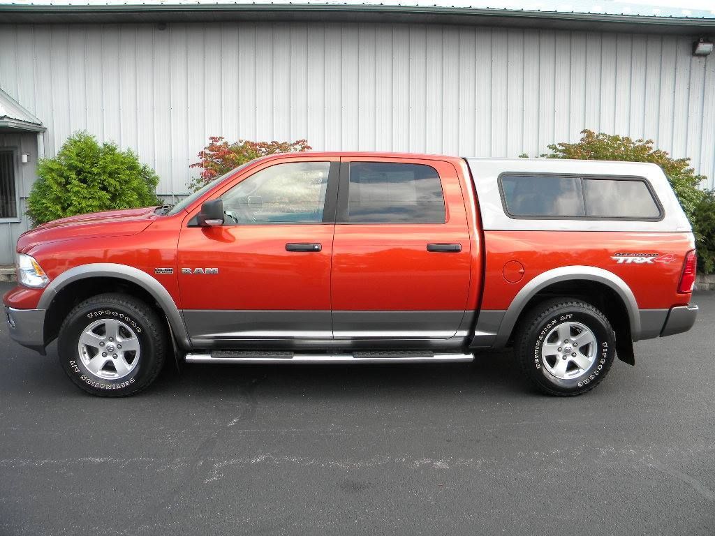 Red and gray Dodge Ram pickup truck with a white camper shell parked outdoors.