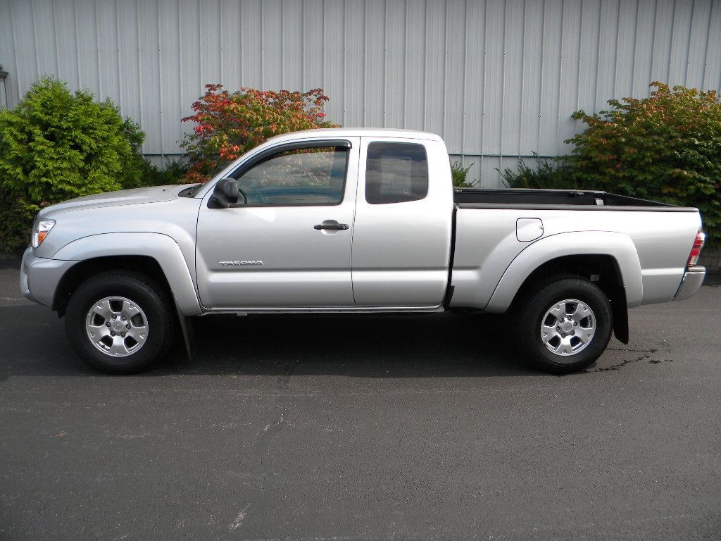 Silver Toyota Tacoma pickup truck parked on asphalt in front of a building and greenery.