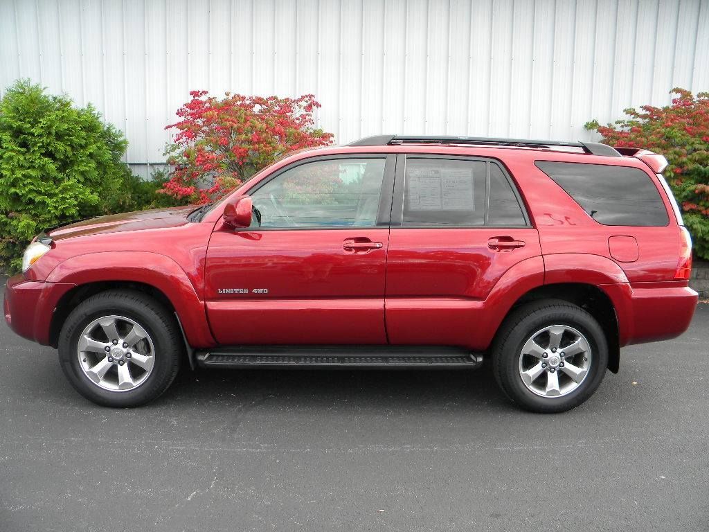 Red Toyota 4Runner SUV parked on asphalt next to greenery.