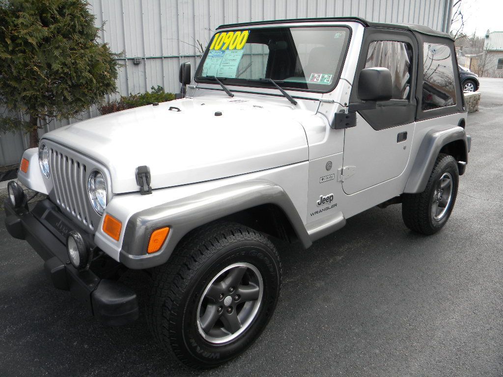 Silver Jeep Wrangler parked in front of a building; soft top on.
