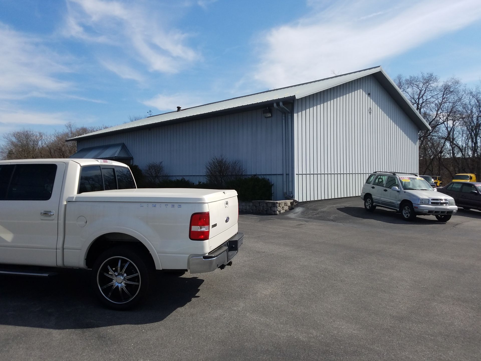 White pickup truck and silver SUV parked outside a metal building on a sunny day.