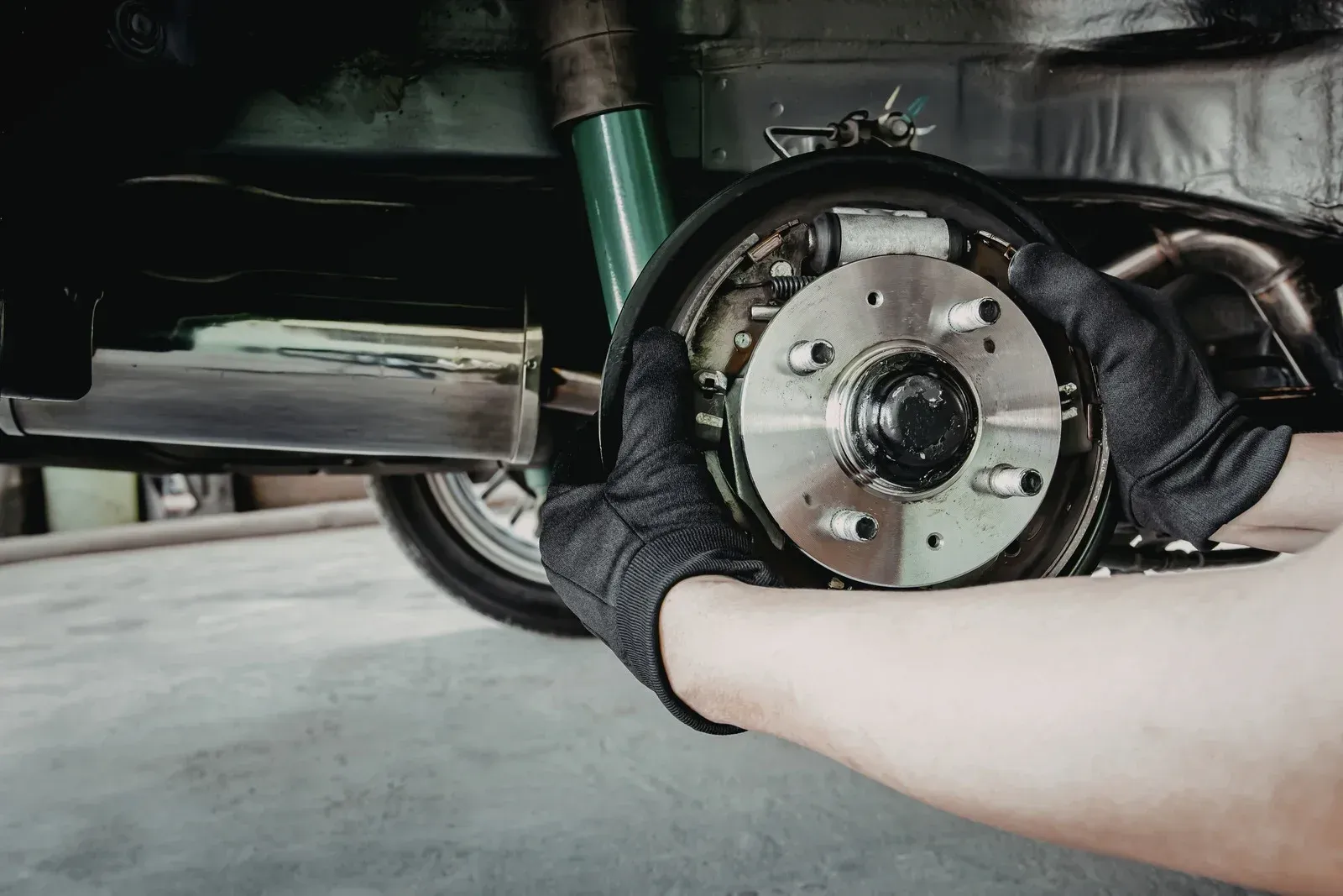 Gloved hands holding a car's brake drum assembly during repair.