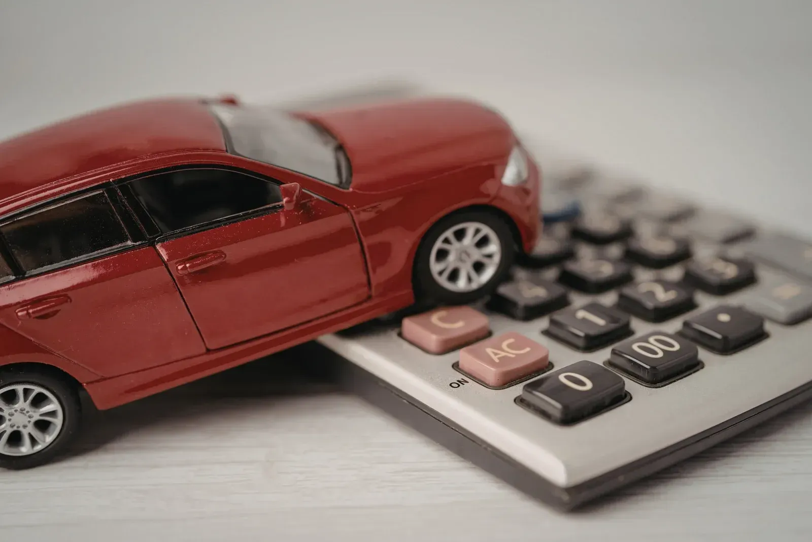 Red toy car on a calculator, symbolizing car expenses or cost analysis.