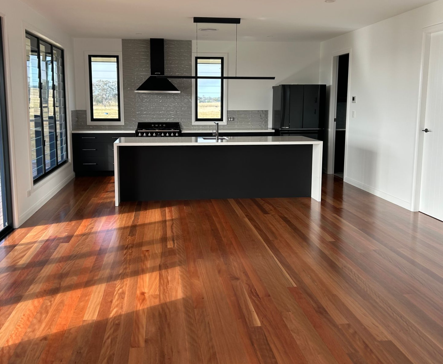 Kitchen with hardwood floors, dark cabinets, a white island, and large windows — C & S Building Pty Ltd In Bentley, NSW