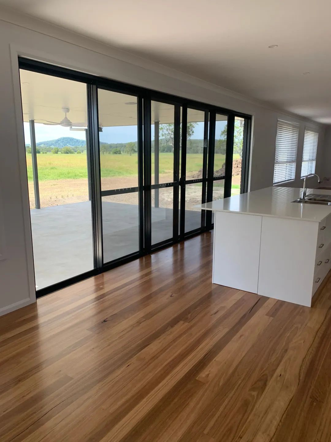 Interior with wood floor, white kitchen island, and large black-framed glass doors opening to a patio — C & S Building Pty Ltd In Bentley, NSW