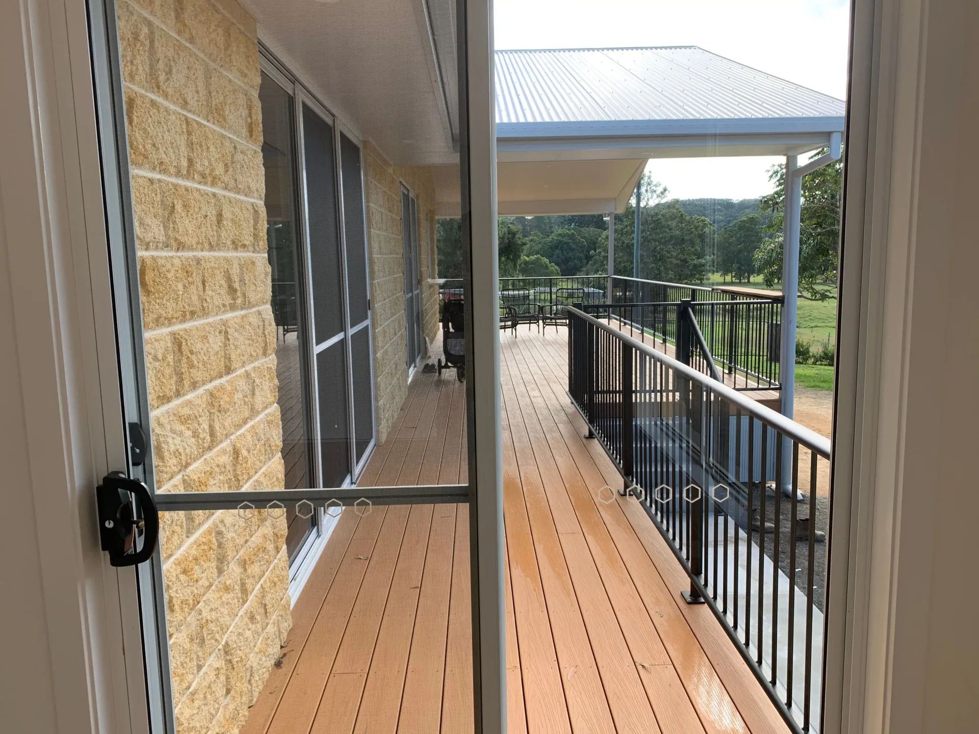 View from inside a house to a wooden deck with black railing and covered patio — C & S Building Pty Ltd In Bentley, NSW