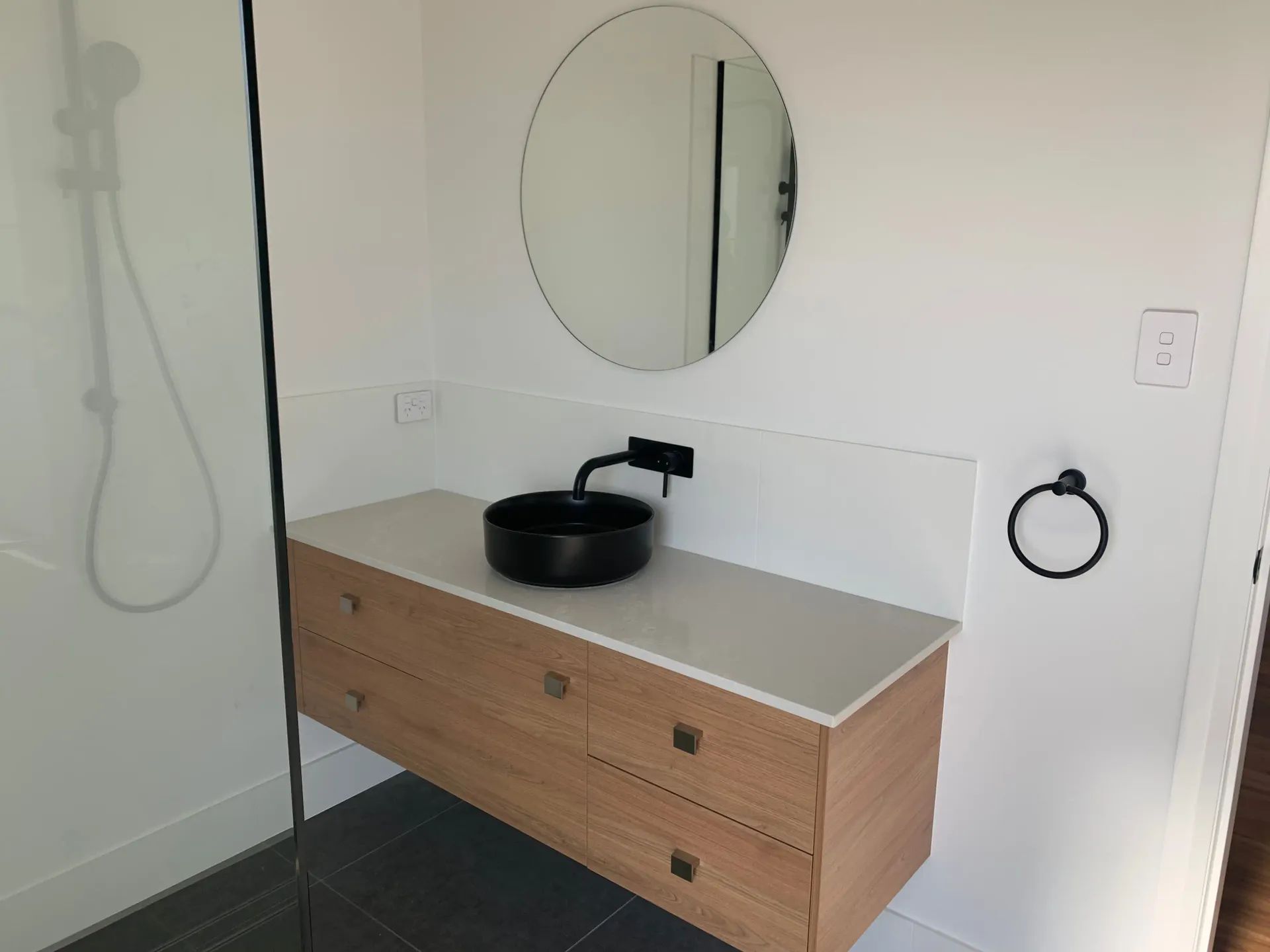 Floating Wooden Vanity with Black Sink and Round Mirror in A Bathroom — C & S Building Pty Ltd In Bentley, NSW