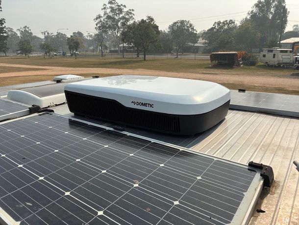 Solar panels and a black and white rooftop air conditioner on a vehicle, outdoor setting.