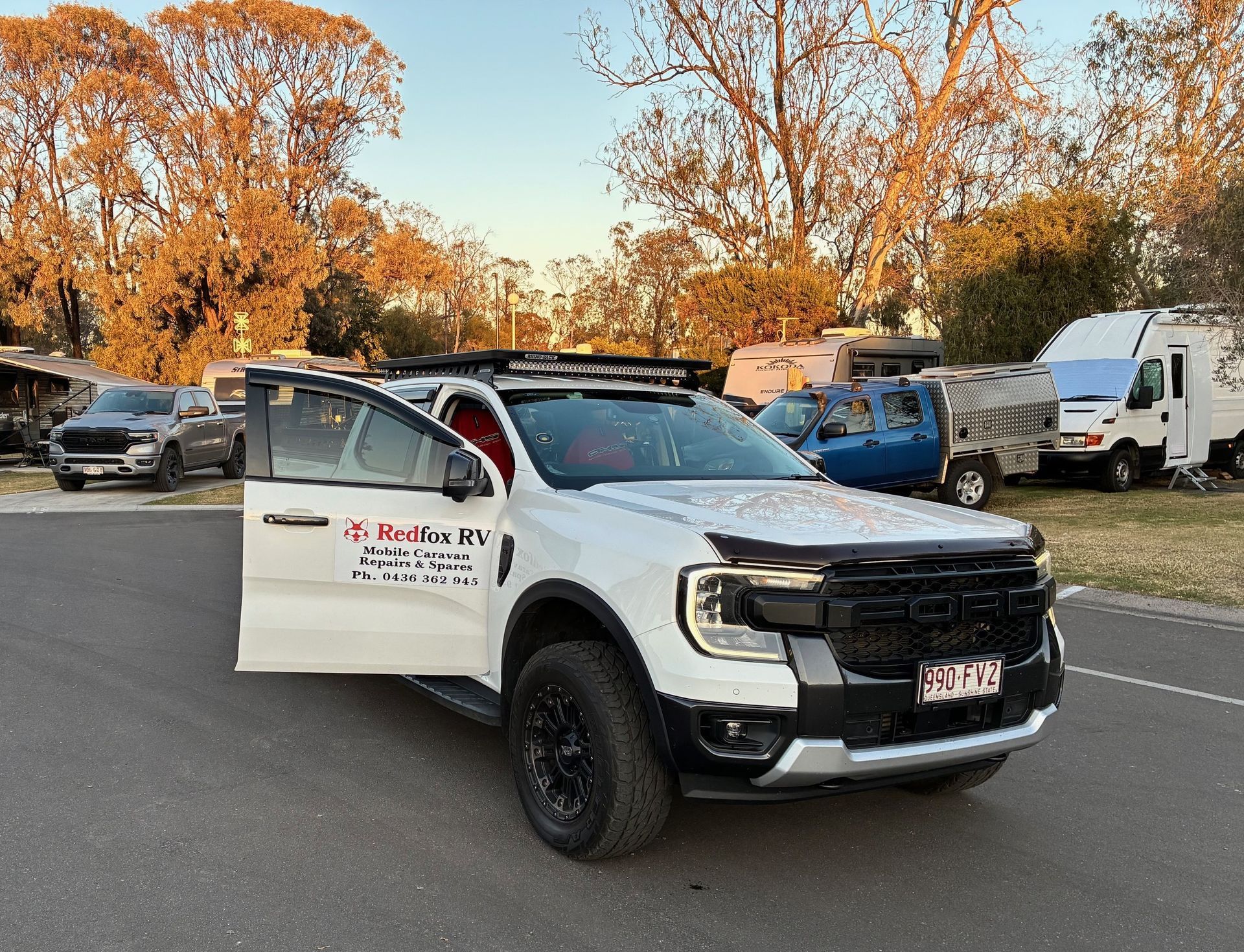 White pickup truck with open door, parked outside with RVs in the background.