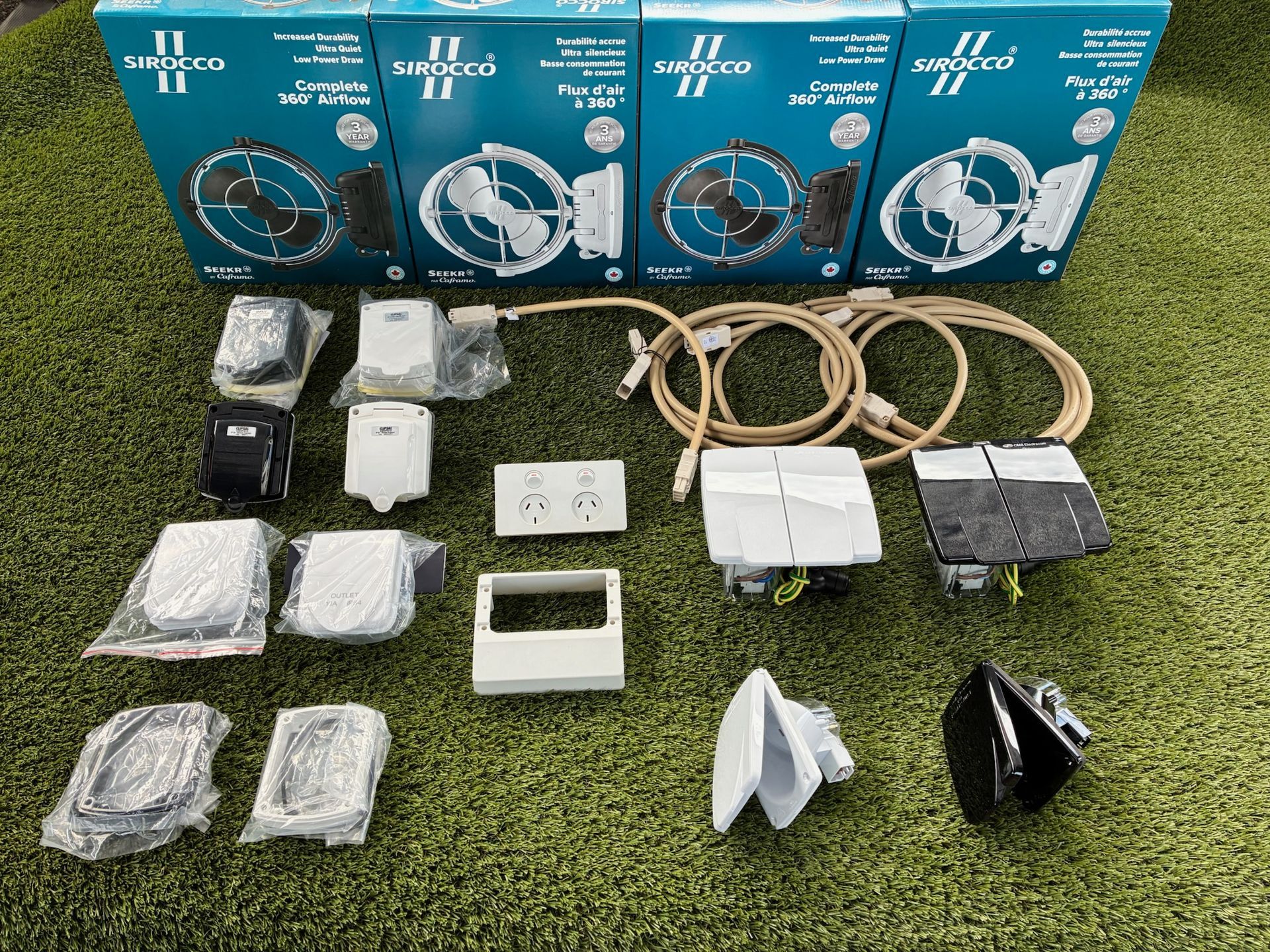 Assortment of electrical components including fans, outlets, and wiring laid on green turf, with boxes visible.