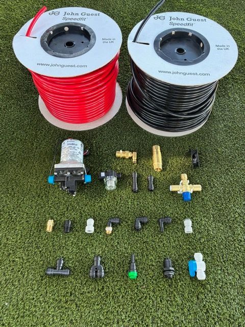 Plumbing components: spools of red and black tubing, pump, and various fittings, laid out on grass.