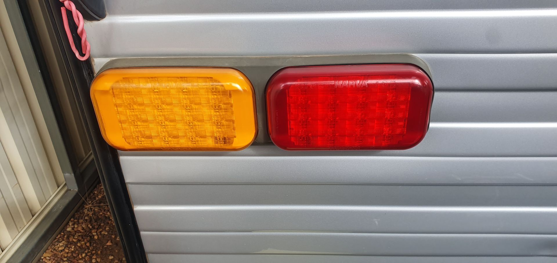 A close-up shows two rectangular trailer lights, yellow and red, mounted on silver siding.