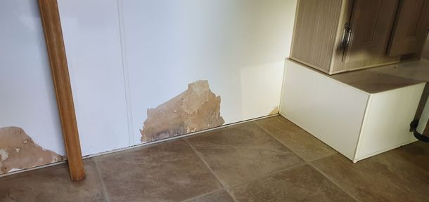 Damaged wall corner with peeling paint, brown floor, and a wooden post.