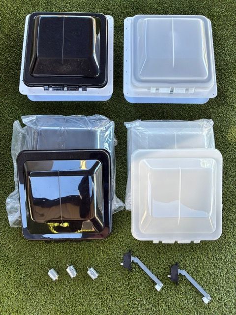 Four black and clear square roof hatches  and mounting hardware on grass.