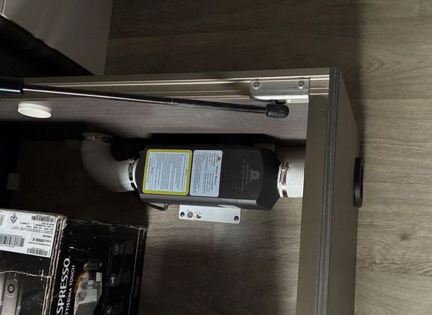 Diesel heater installed in a cabinet. Silver exhaust pipe, black heater body with blue and yellow labels.