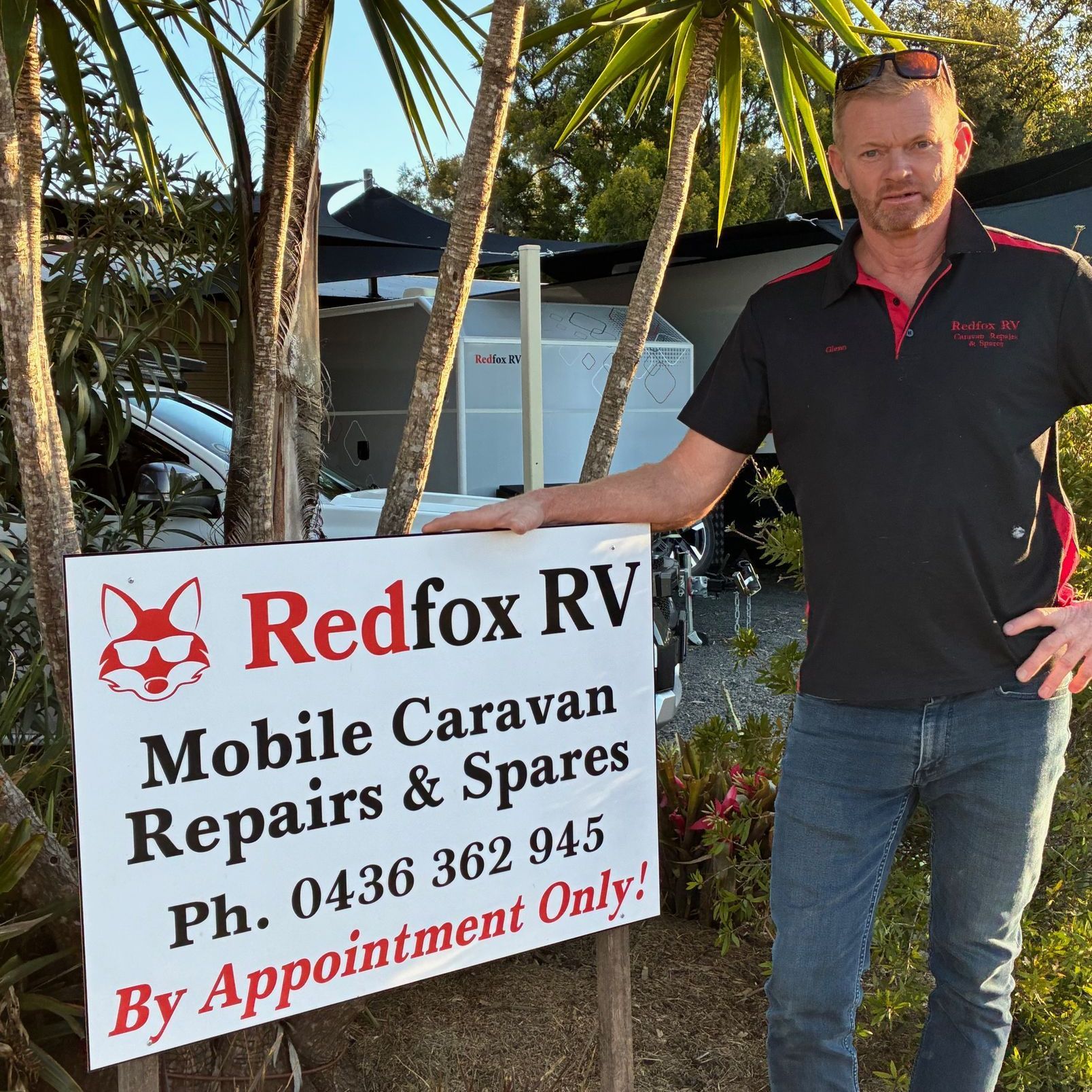 Man in Redfox RV shirt stands next to a sign offering mobile caravan repairs.