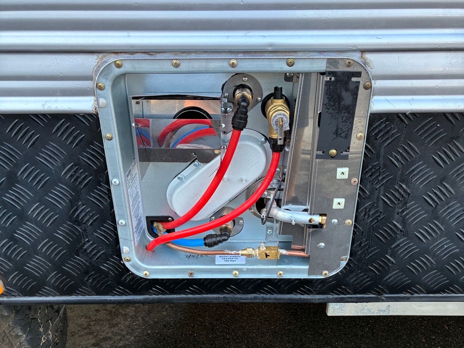 Water heater access panel on a caravan, showing pipes and components.