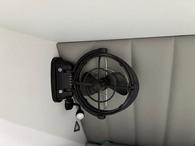 Black wall-mounted fan with light fixture, angled against a white wall with a grey backdrop.