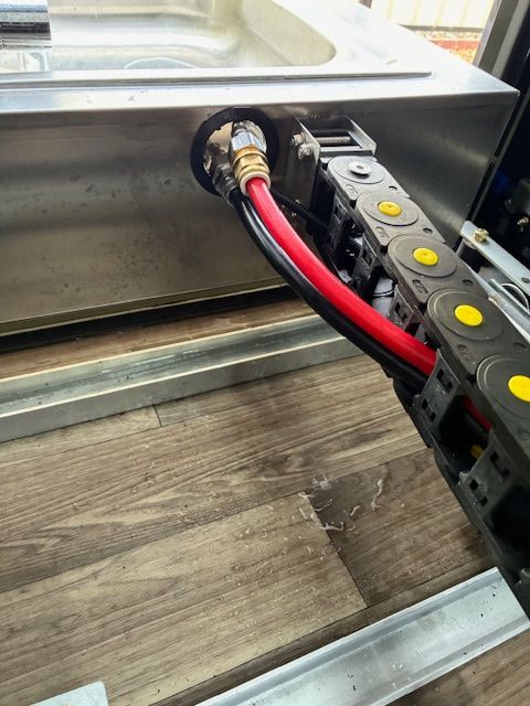Red and black cables exiting a metal container through a hole, encased in a black plastic chain.