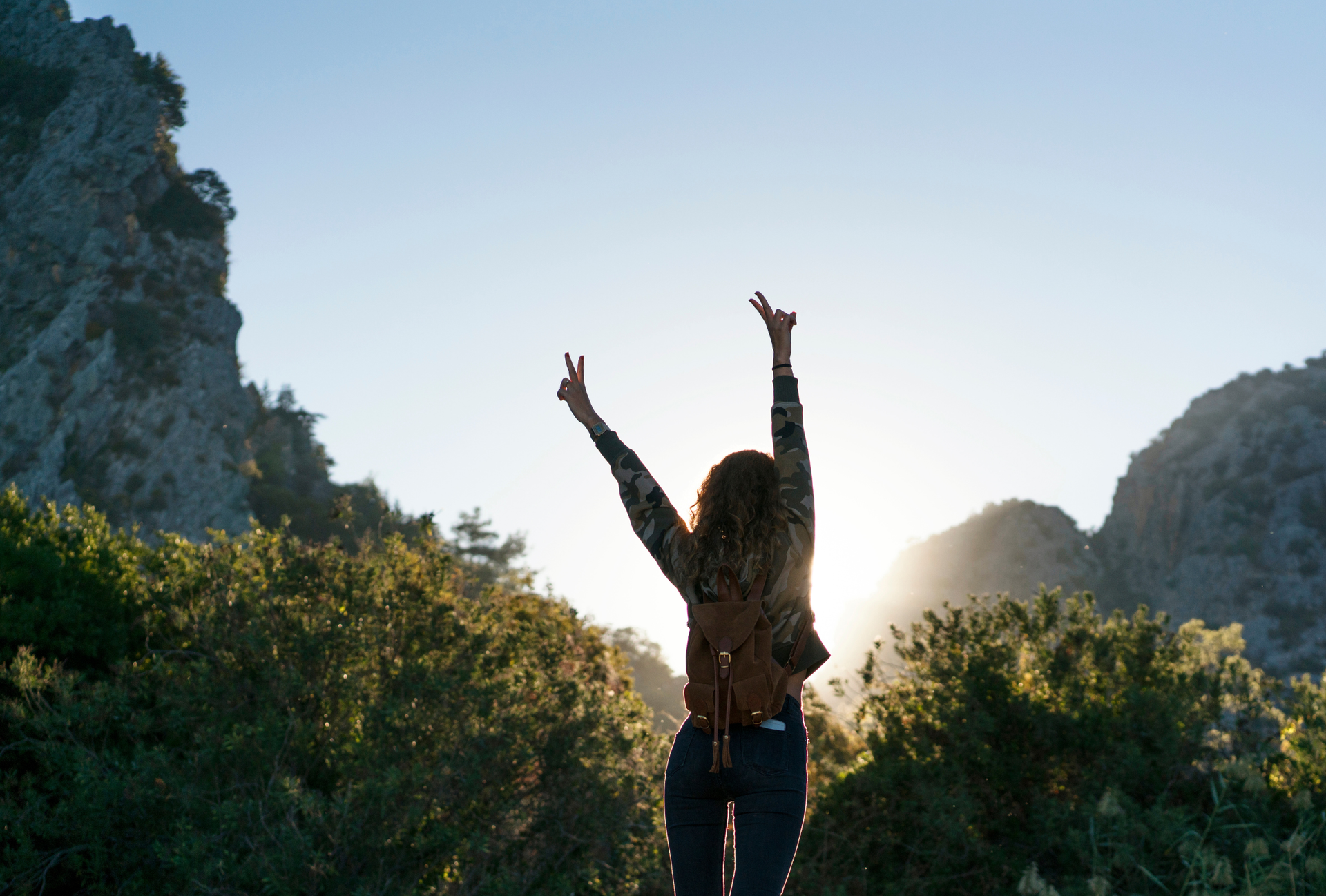 A woman is standing on top of a mountain with her arms in the air.
