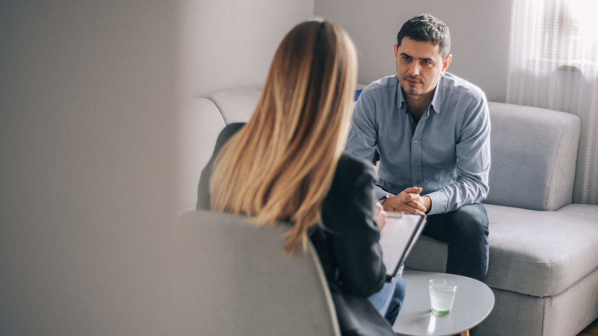 A man and a woman are sitting on a couch talking to each other.