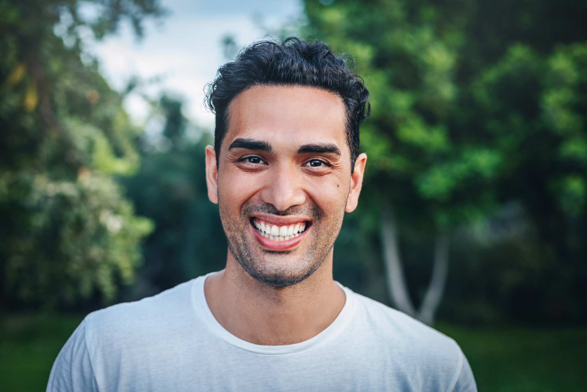 A young man is smiling for the camera in a park.