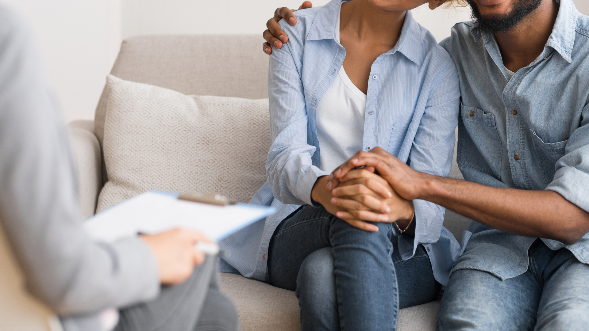 A couple sits together, holding hands during a therapy sessoin.
