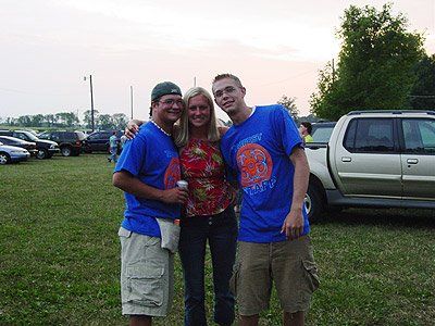 Two men and a woman are posing for a picture in a parking lot.
