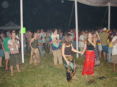 A group of people are dancing in the grass under a tent