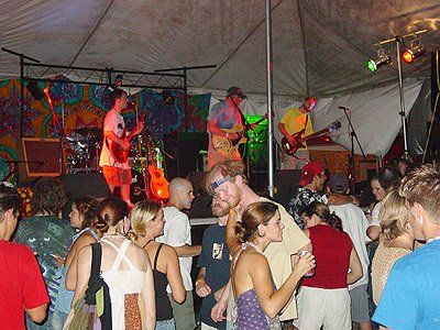A group of people are dancing in front of a stage with a man playing a guitar