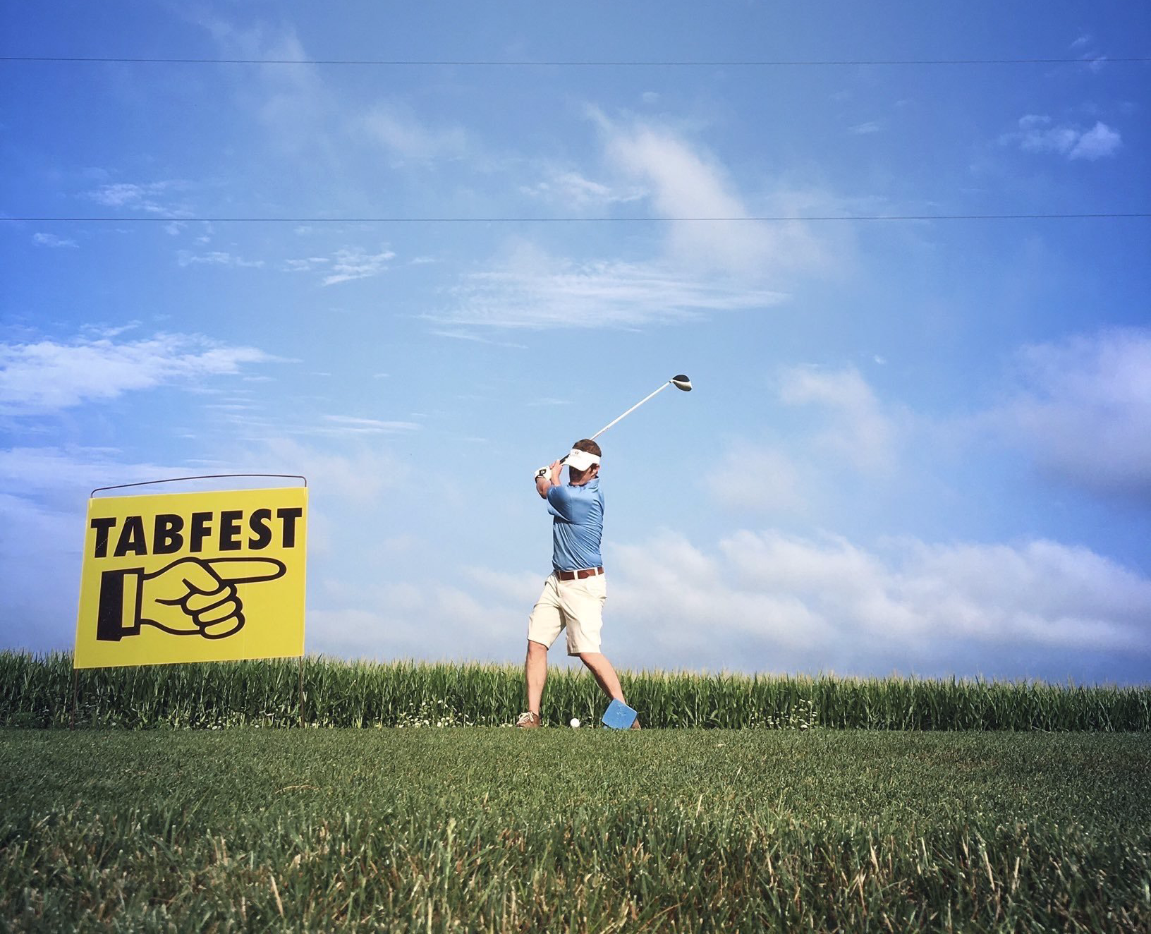 A man swings a golf club in front of a tabfest sign