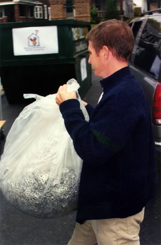 A man is carrying a bag of garbage in front of a dumpster
